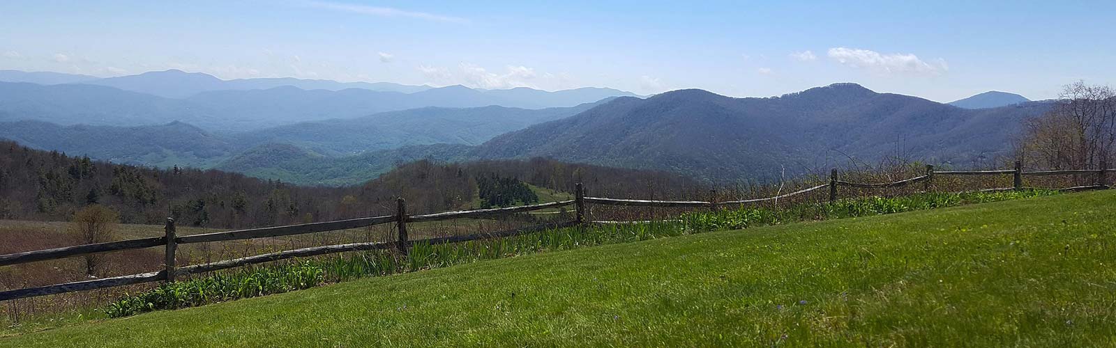 A green field with a rustic fence and mountains in the background